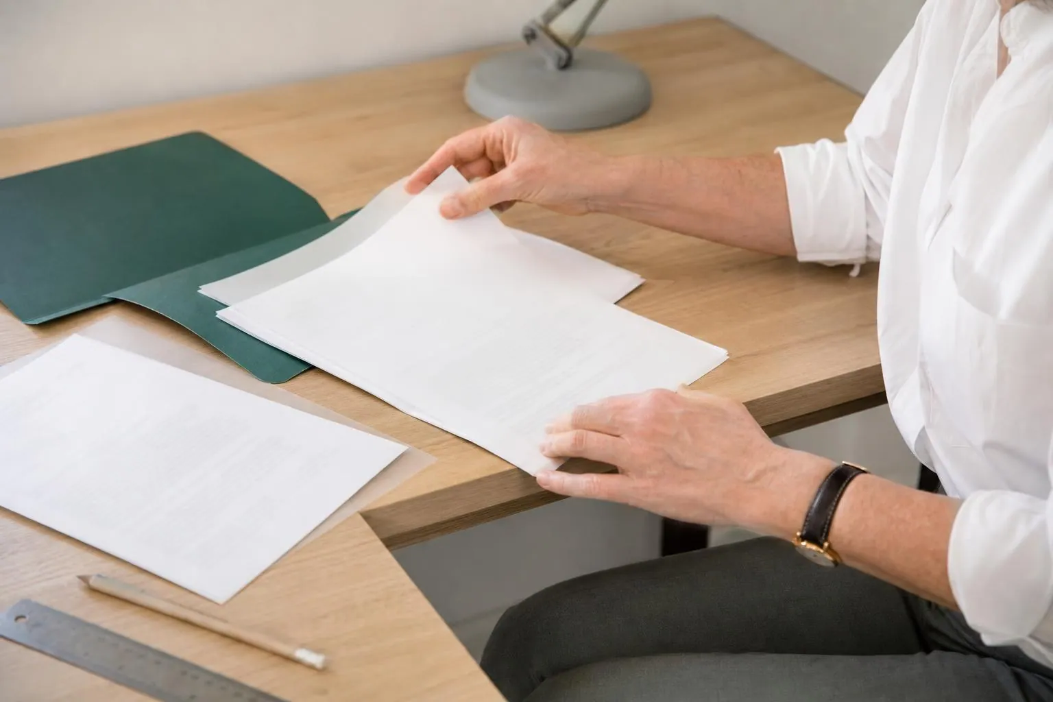 Mains d une professionnelle feuilletant des statuts de societe agrafes posees sur une table de bois clair a cote d une chemise verte